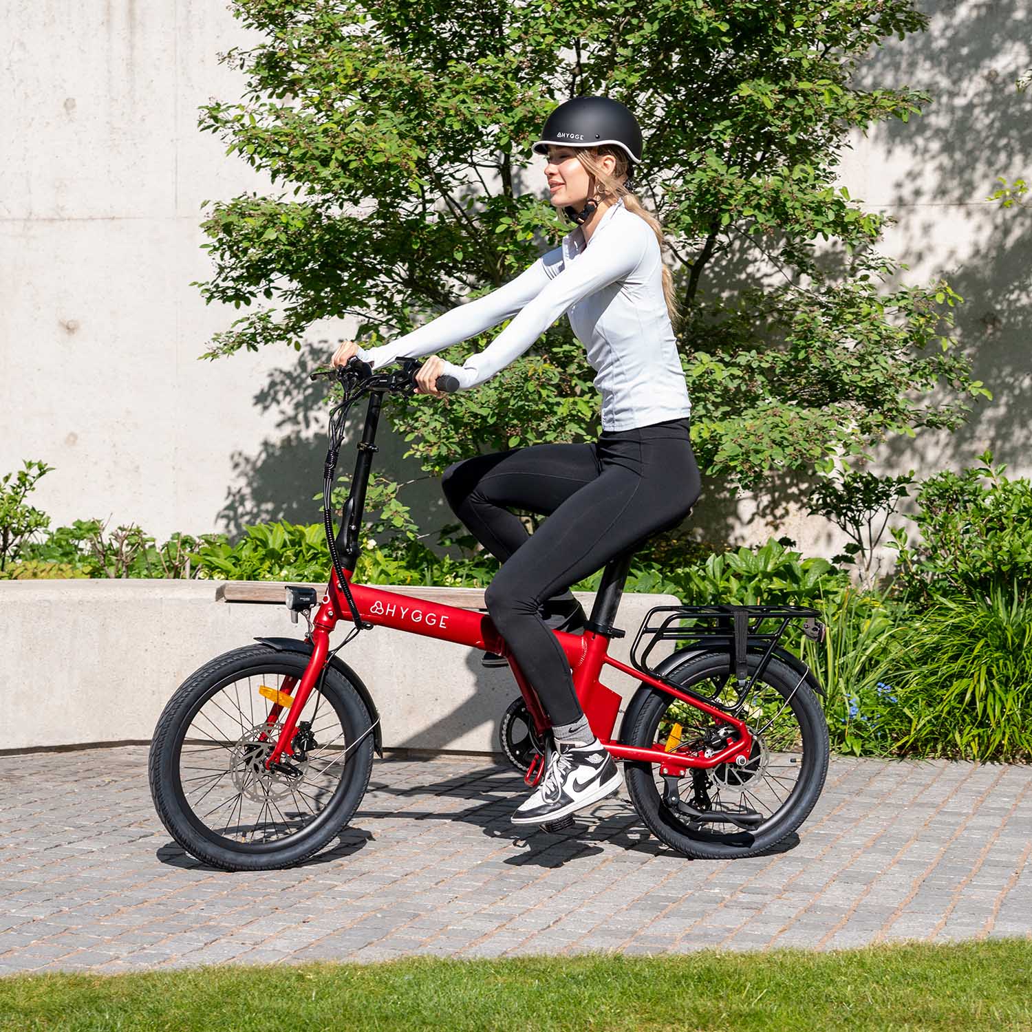 Woman riding sangria red Hygge Virum lightweight folding e-bike in urban setting with greenery
